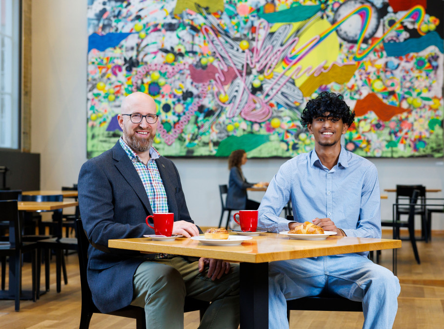 Zwei Männer sitzen vor einem bunten Gemälde an einem Tisch mit Kaffee
