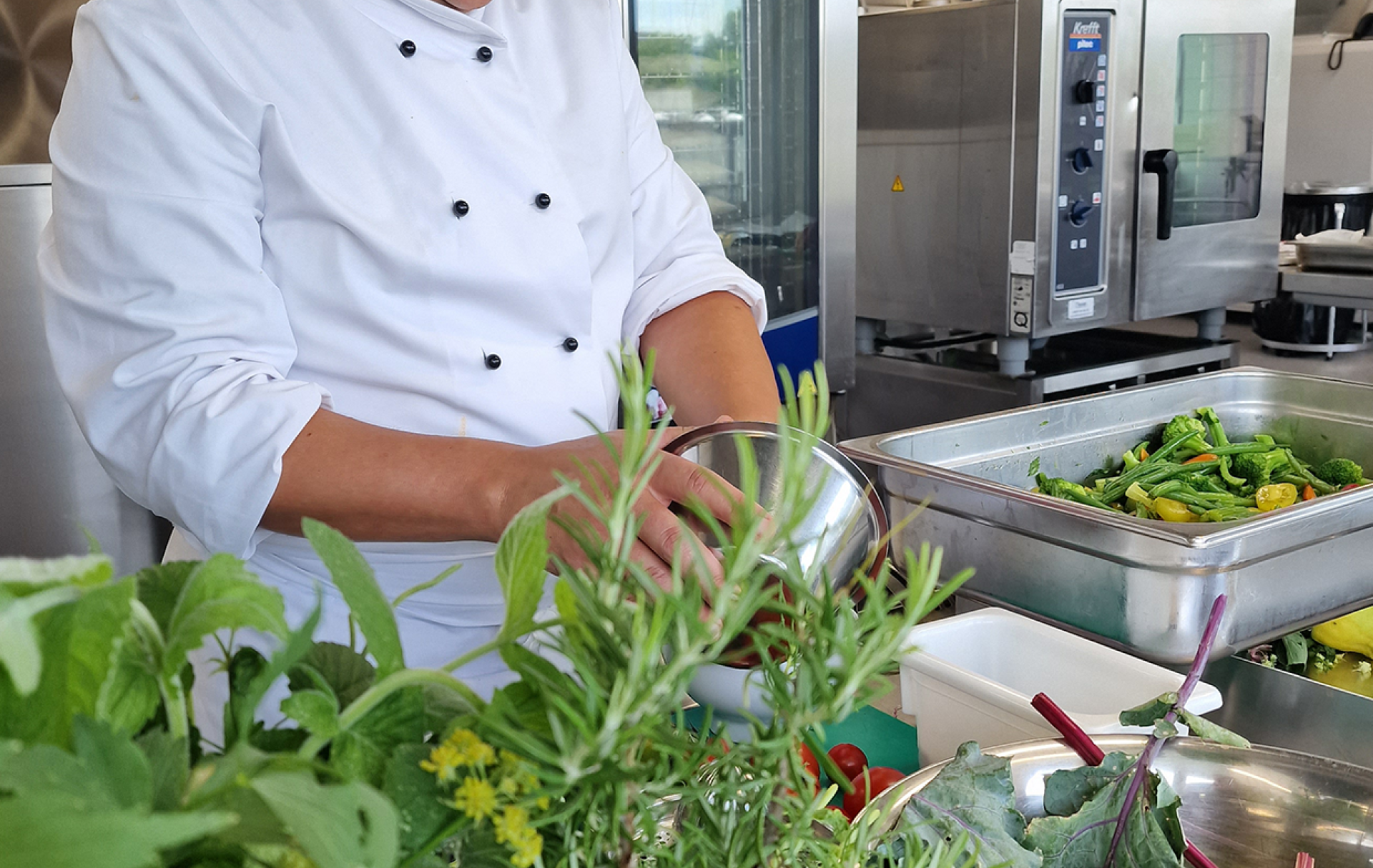 Koch in Küche bei der Zubereitung von Essen mit frischen Kräutern im Hintergrund