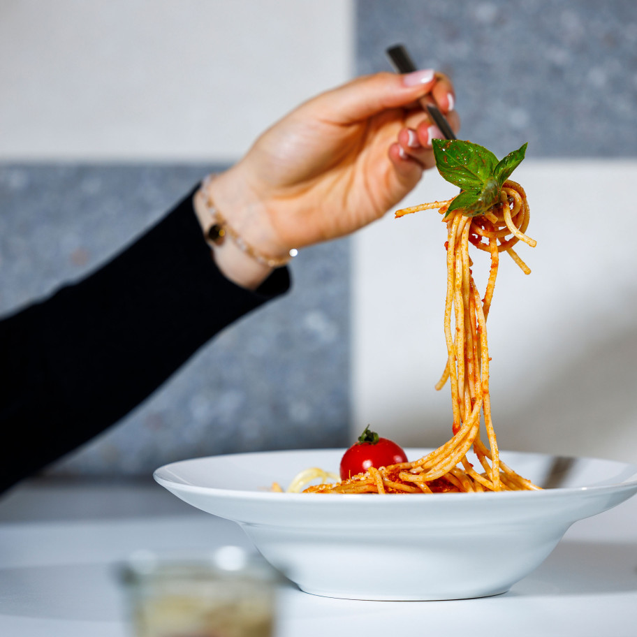 Weibliche Hand hält eine aufgedrehte Gabel Spaghetti über einen Teller