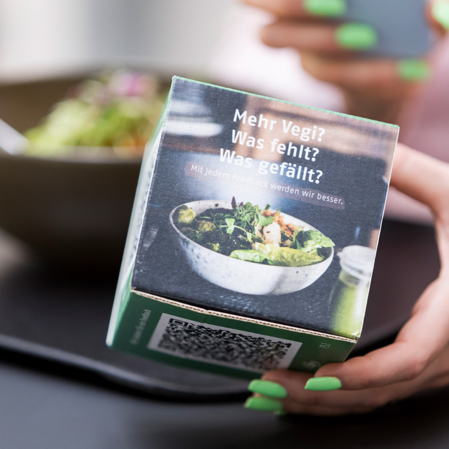 Kartonwürfel für Gästefeedback in einer weiblichen Hand, dahinter eine Bowl