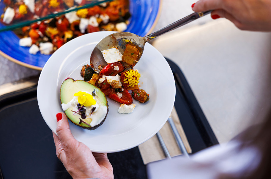 Teller, der am Buffet beladen wird mit Gemüse und Avocado