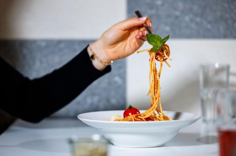 Weibliche Hand hält eine aufgedrehte Gabel Spaghetti über einen Teller