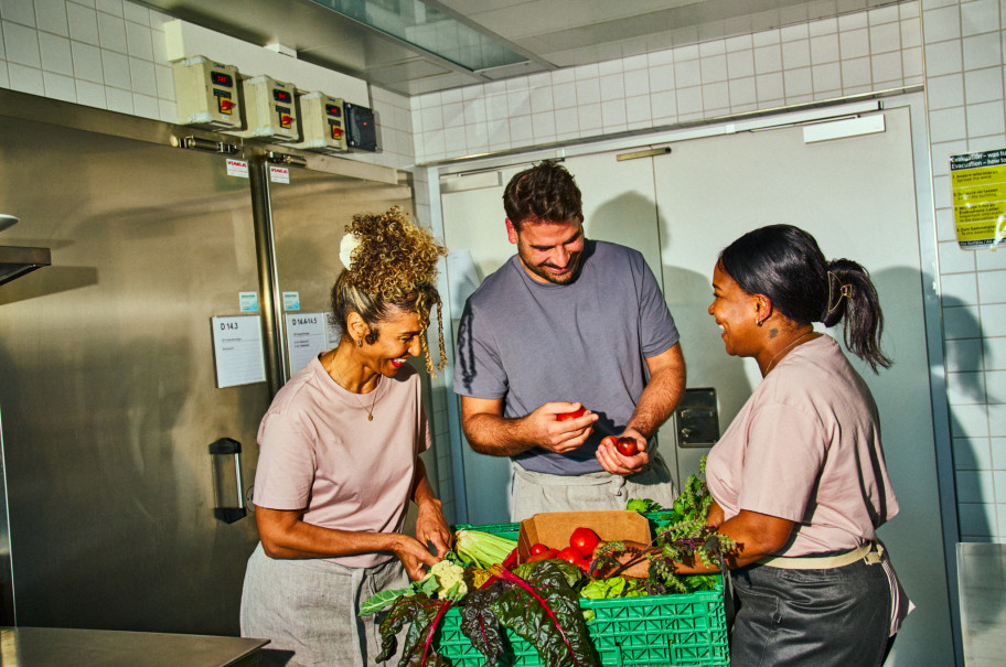 Zwei Frauen und ein Mann stehen in der Küche und rüsten Gemüse.