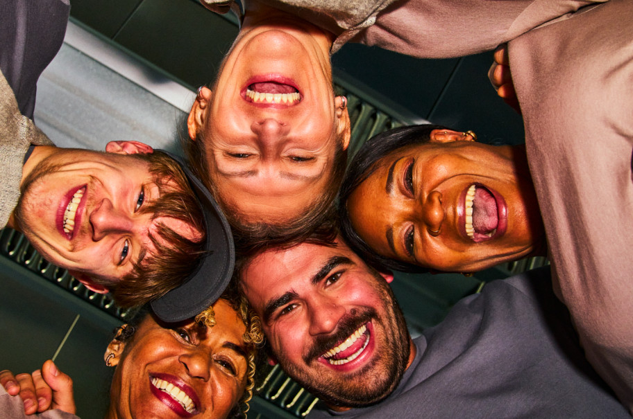 Gruppe von Menschen steht im Kreis und schaut von oben in die Kamera.