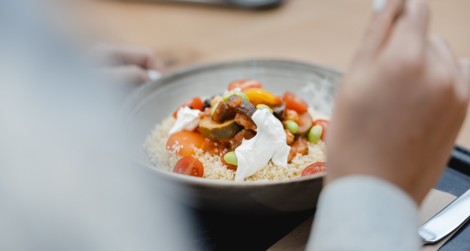 Ein Teller mit Couscous, diversem Gemüse und Joghurt auf einem Tablett