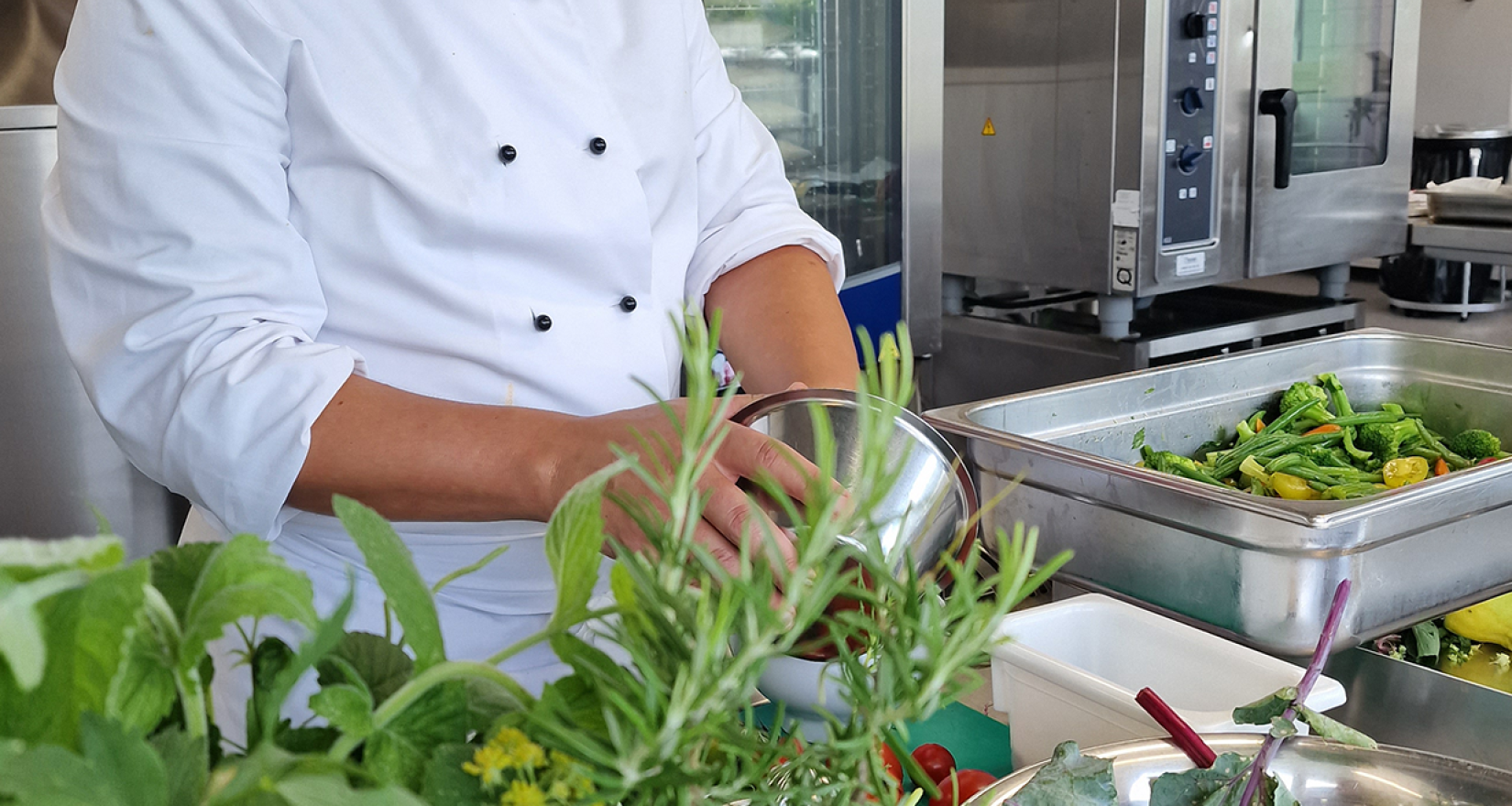 Koch in Küche bei der Zubereitung von Essen mit frischen Kräutern im Hintergrund