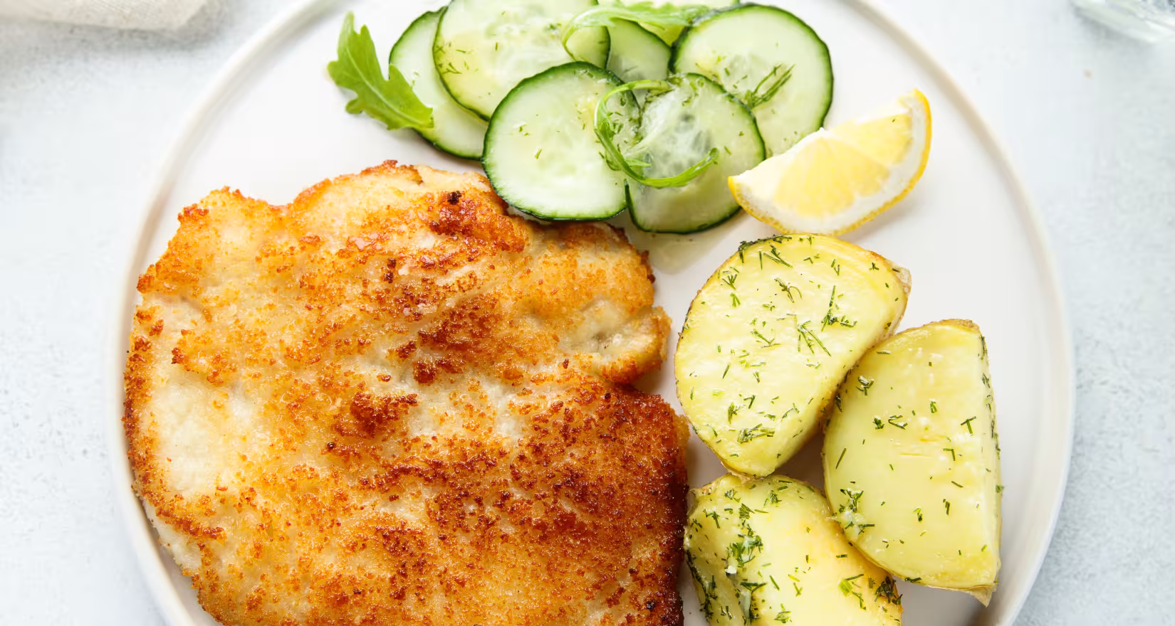 ein Teller mit Schnitzel, Kartoffeln und Gurken