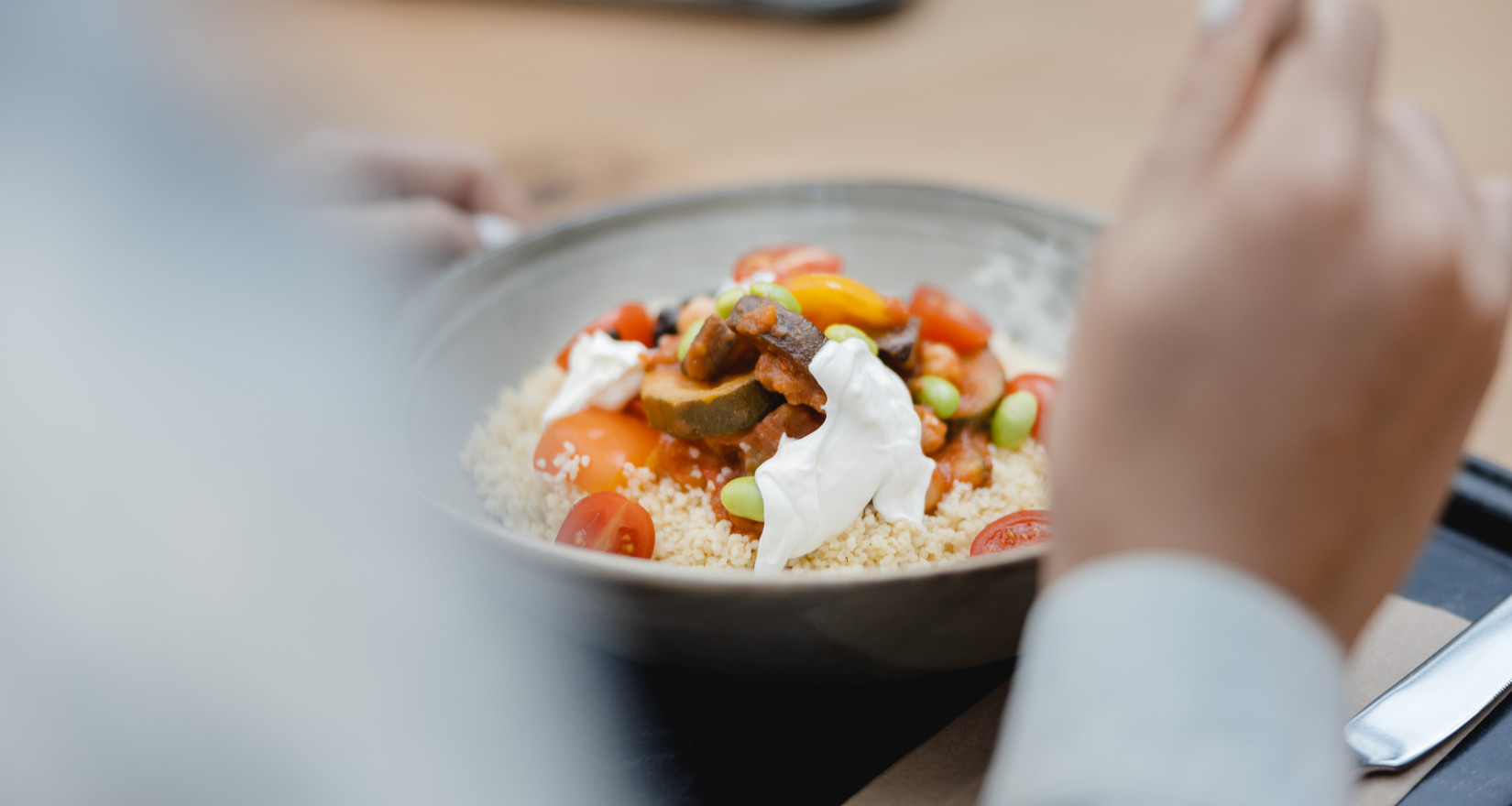 Person isst eine ausgewogene Bowl mit Gemüse und Couscous