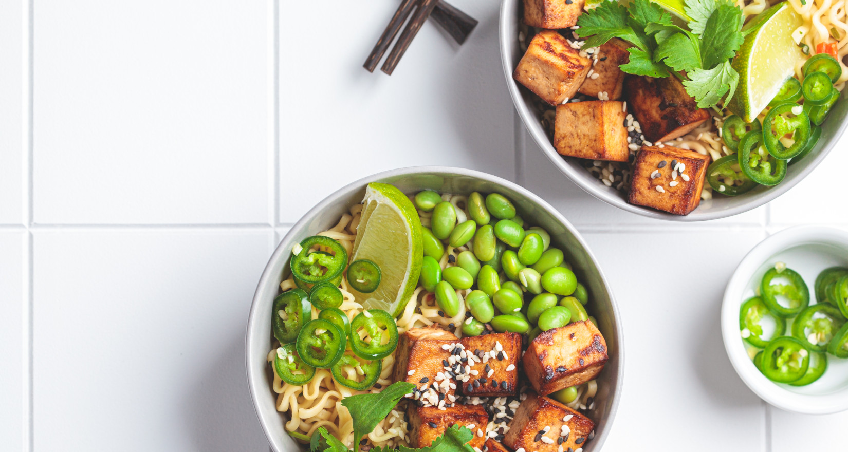 Zwei Bowls mit Nudeln, Tofu, Bohnen und Limetten