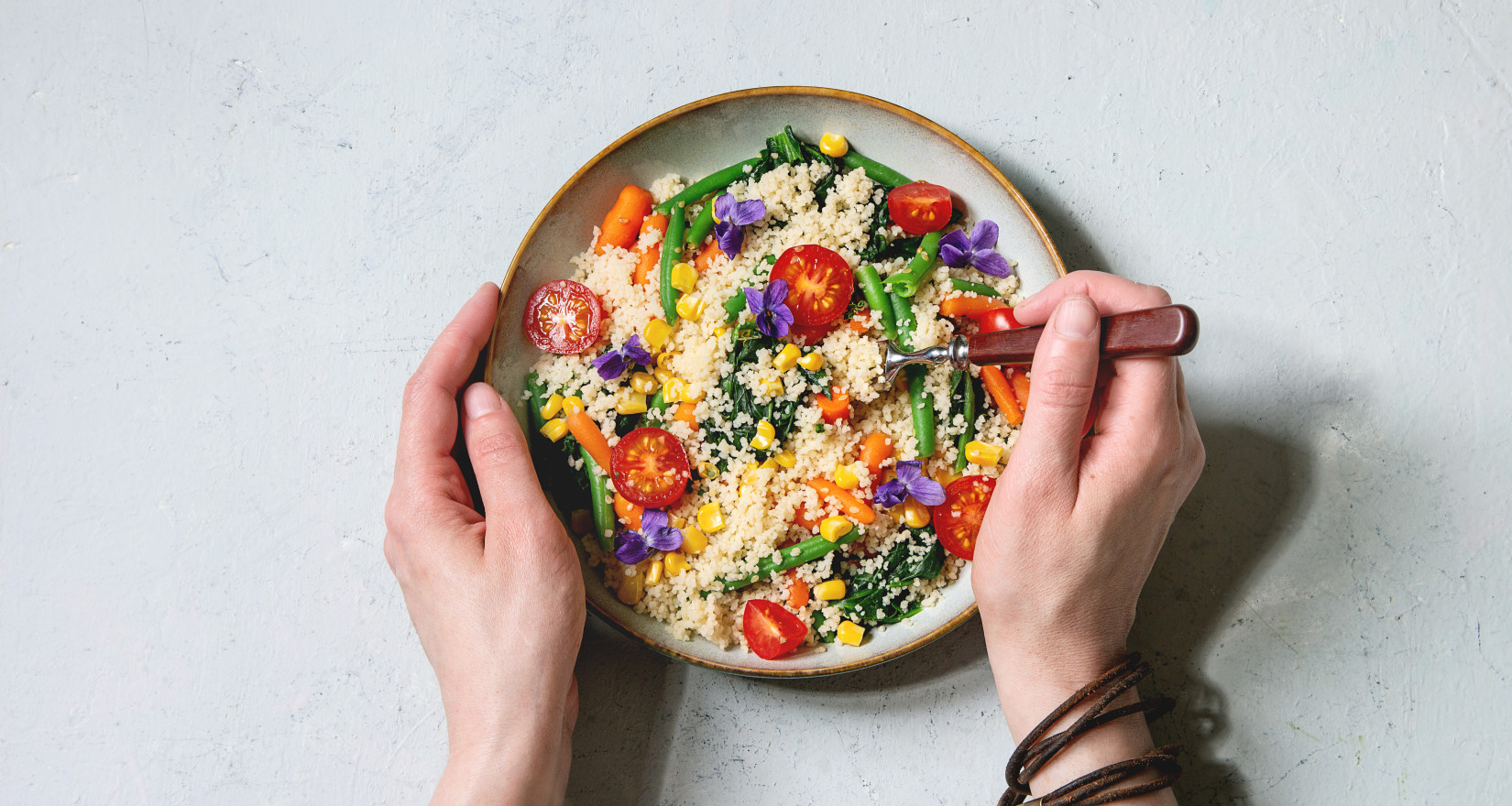 Zwei Hände halten eine Schüssel mit Couscous und diversem Gemüse