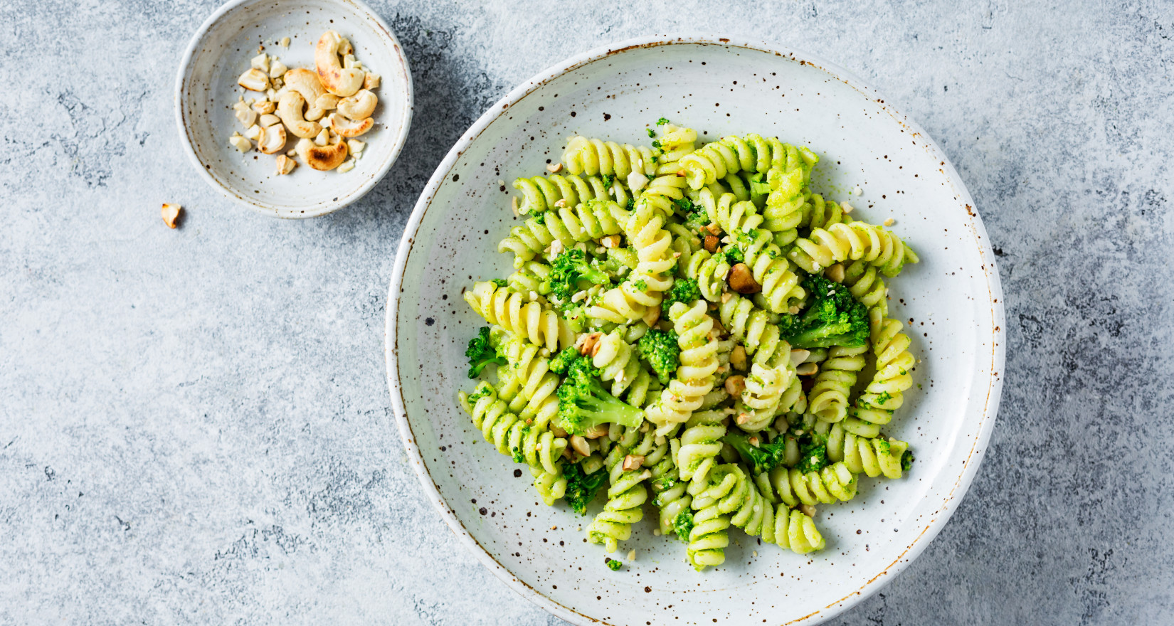 Fusilli mit Broccoli und Cashewnüssen auf einem Teller, daneben eine Schale mit Cashewnüssen