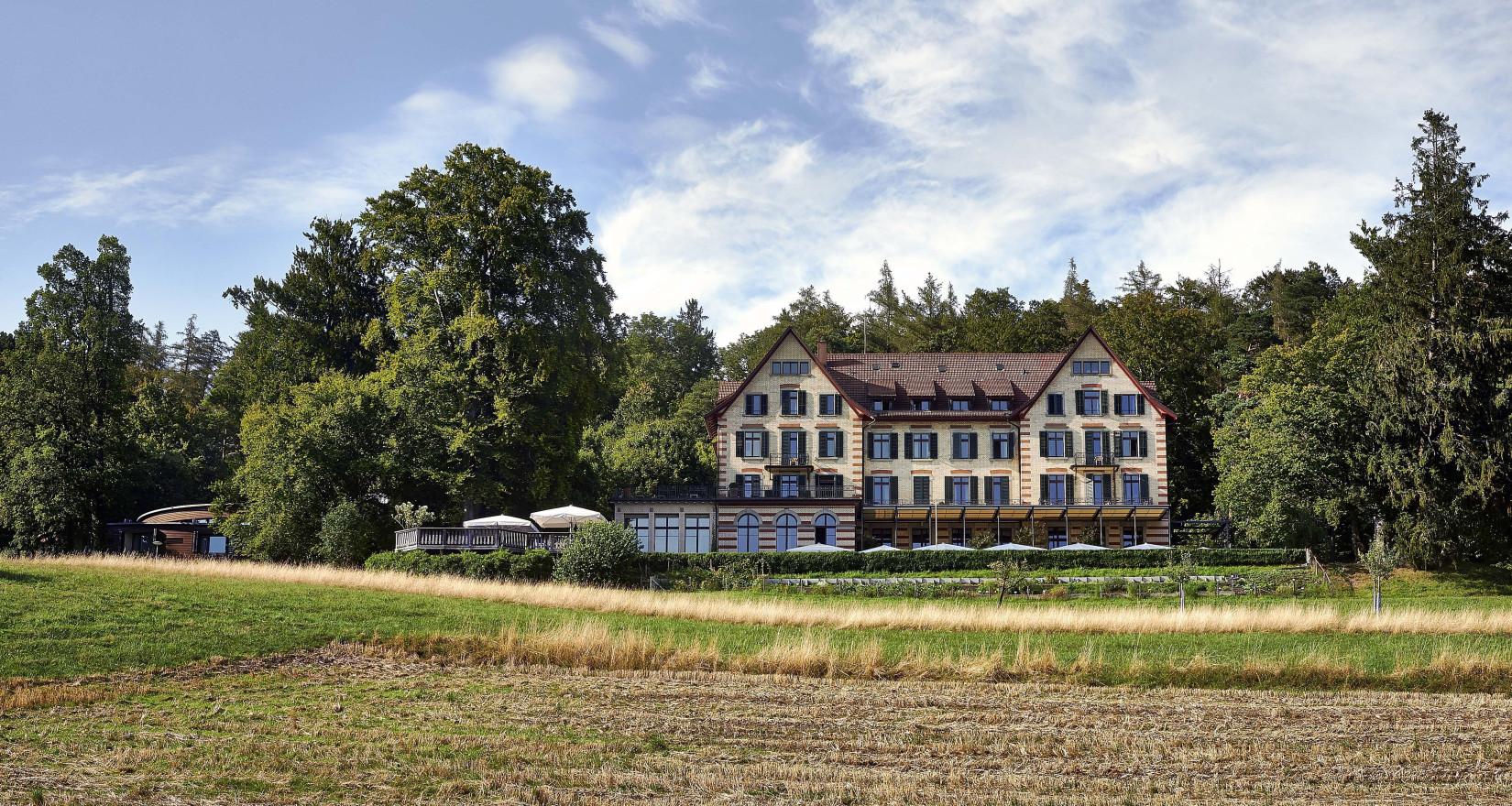 Sorell Hotel Zürichberg von aussen, Ansicht mit opulenten Hochstammobstbäumen dahinter und grünen Wiesen davor