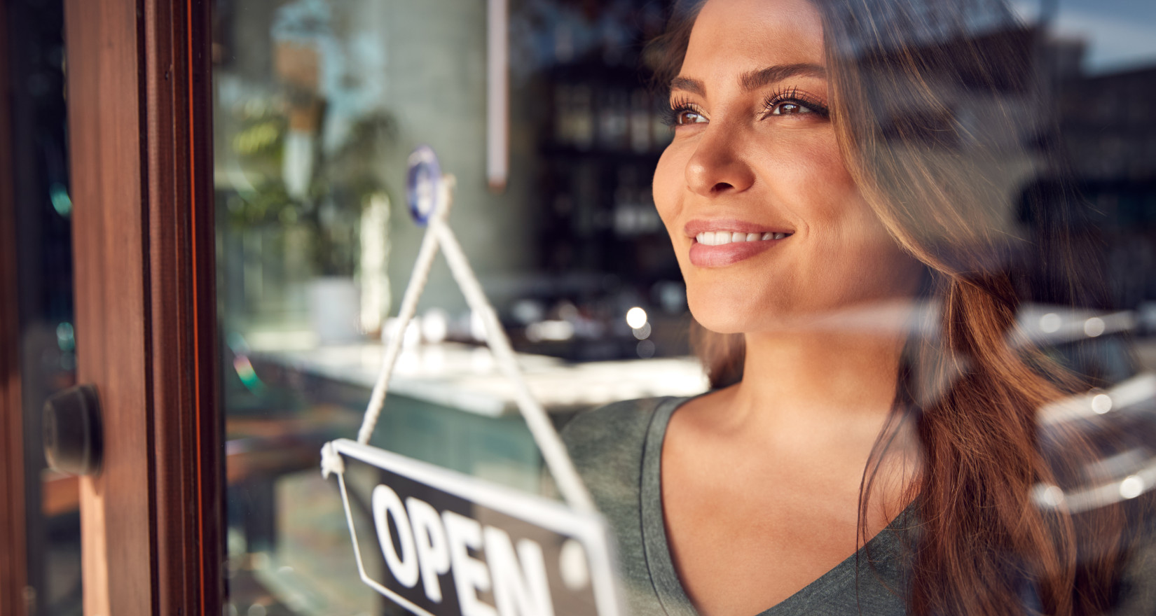 Frau blickt durch eine Fensterscheibe, vor ihr ein Openschild