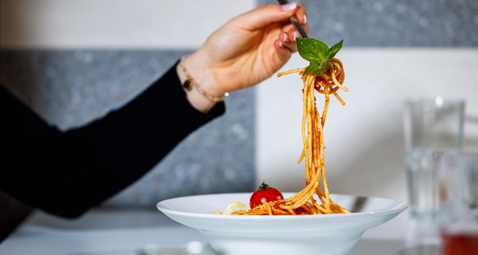 Weibliche Hand hält eine aufgedrehte Gabel Spaghetti über einen Teller