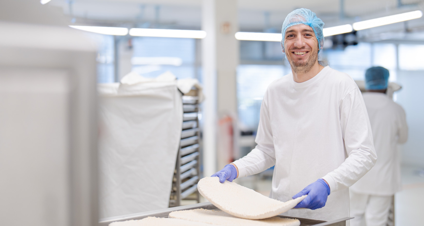 Mann mit Produktionskleidung und Kopfhaube steht vor einer Produktionsmaschine