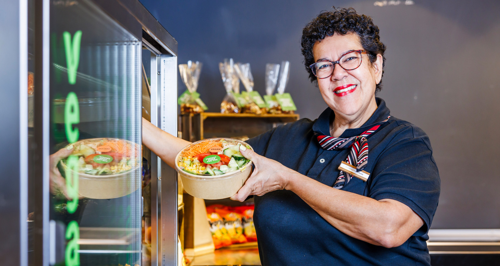 Frau nimmt einen Salat zum Mitnehmen aus einer Kühlvitrine