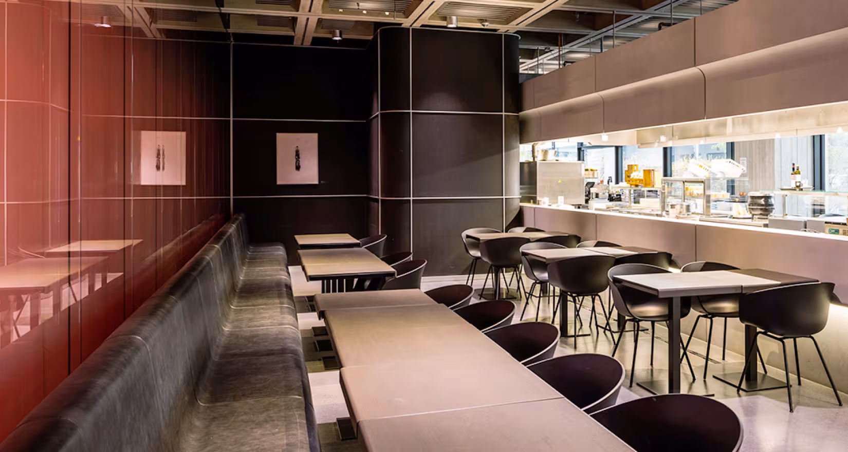 Innenansicht des SRF-Live Restaurants mit Glaswand direkt zum Studio. Einrichtung ist modern mit dunklen Tischen und Stühlen.