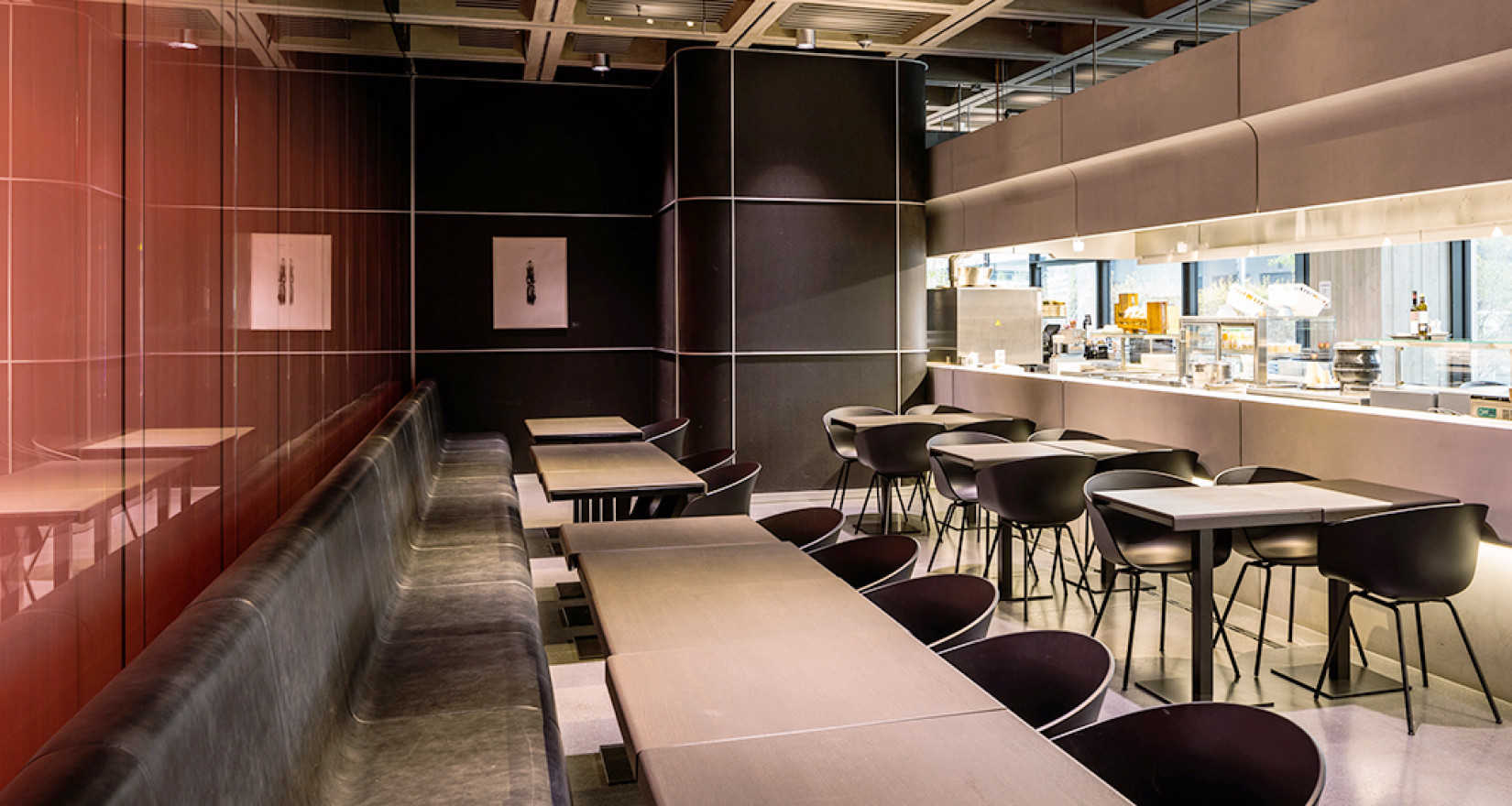 Innenansicht des SRF-Live Restaurants mit Glaswand direkt zum Studio. Einrichtung ist modern mit dunklen Tischen und Stühlen.