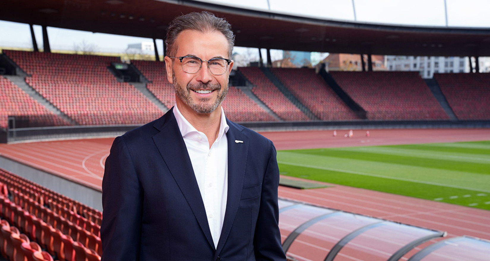 Herr steht im Anzug in einem Schweizer Stadion