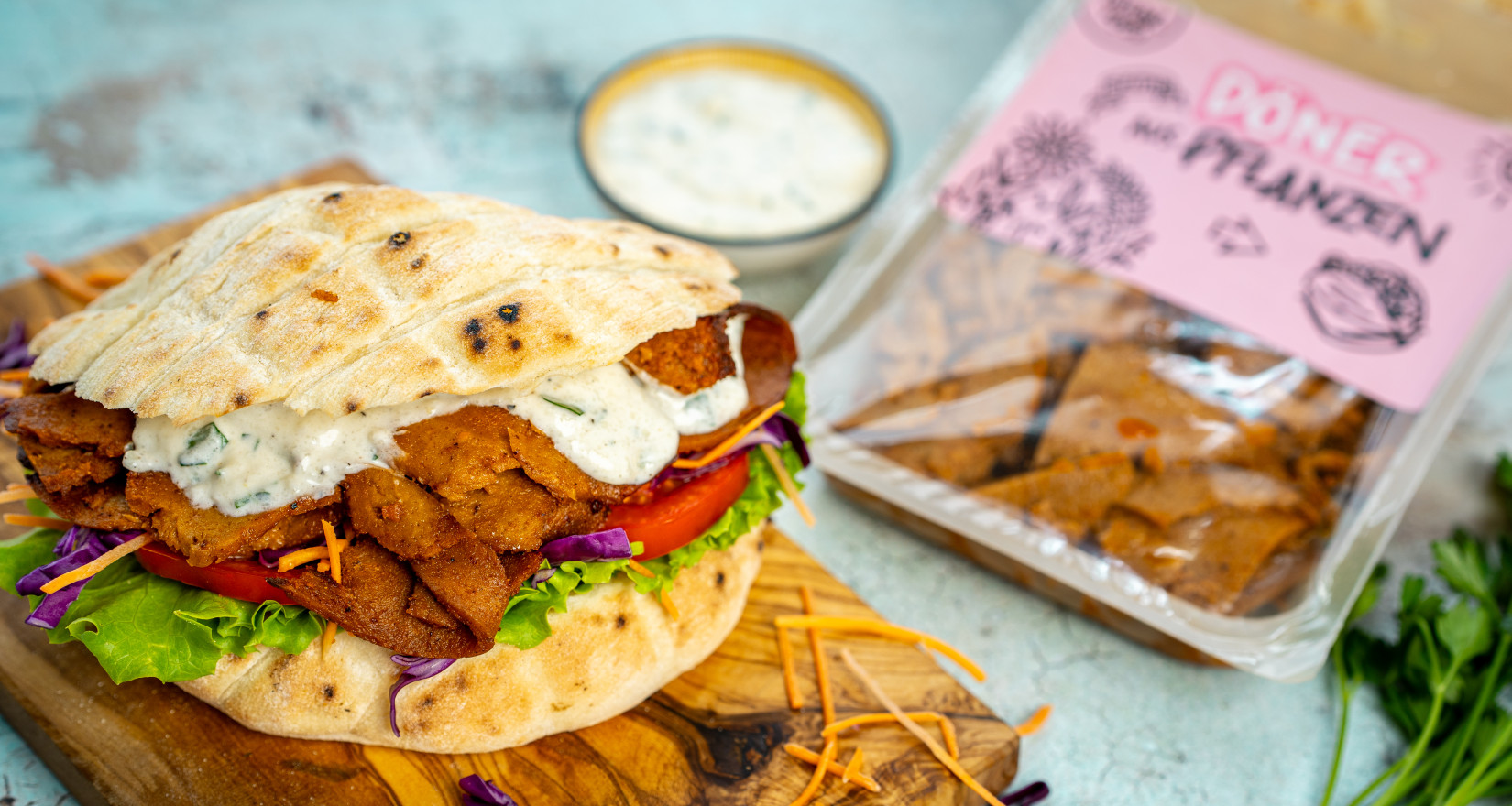 Pflanzenbasierter Döner mit Brot, dahinter eine Verpackung mit der Aufschrift Outlawz Food