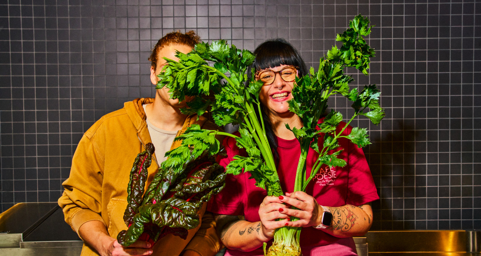 Frau und Mann sitzen in der Küche und halten Gemüse in der Hand.