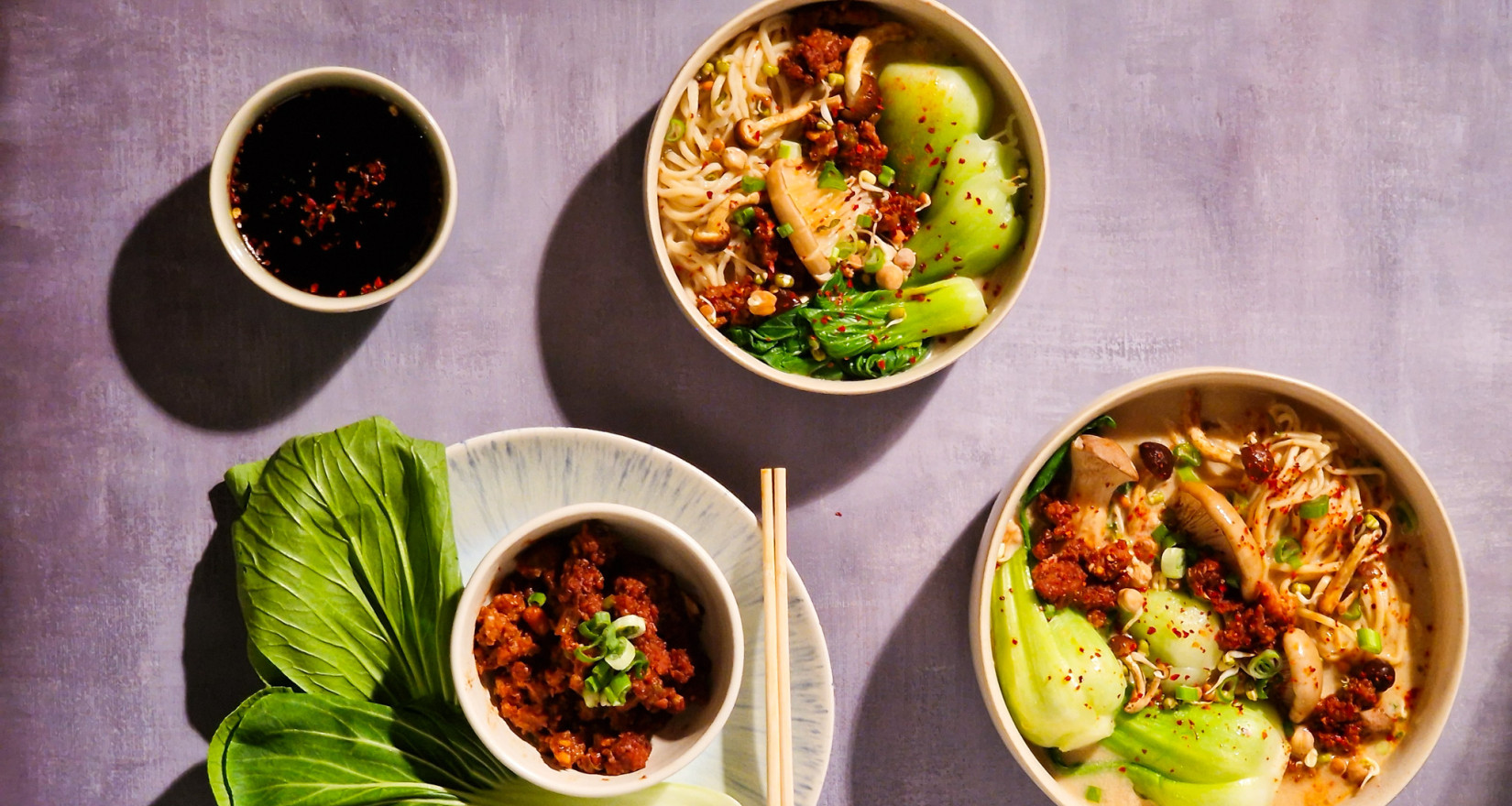 Zwei Schüsseln mit Ramen sowie eine mit Fleisch und eine mit Sojasauce