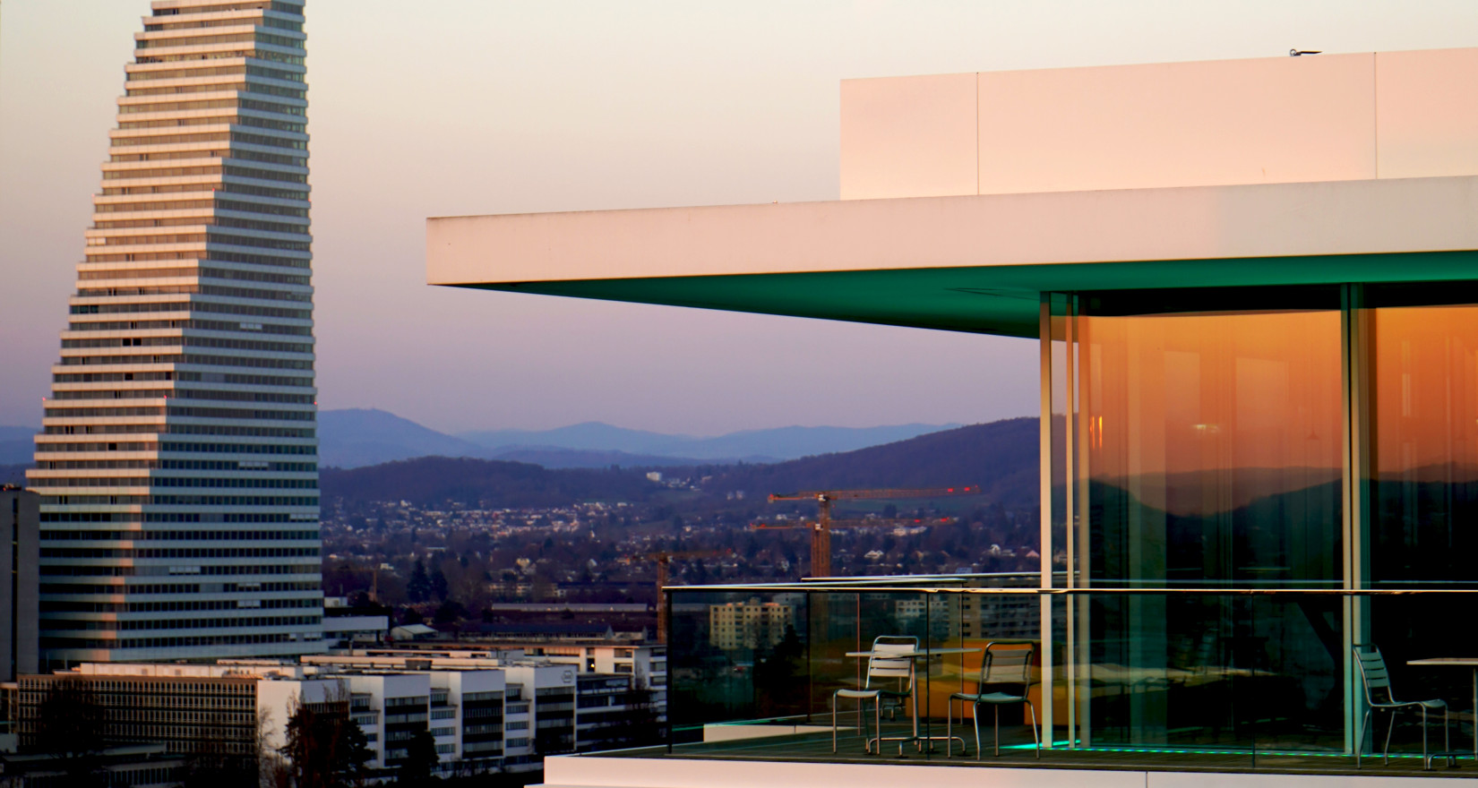 Ansicht Dachterrasse des B1 Rooftop Bistros in Basel bei Sonnenuntergang und den Rôche Türmen im Hintergrund