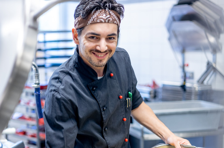 Junger Mann in schwarzer Kochuniform schöpft Pasta aus einem Gastrotopf