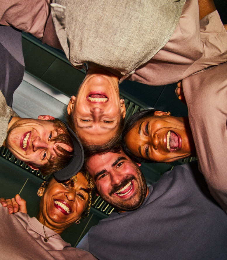 Gruppe von Menschen steht im Kreis und schaut von oben in die Kamera.