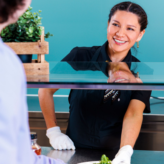 Junge Frau reicht einen Teller mit vegetarischem Gericht über einen Tresen zu einem Mann