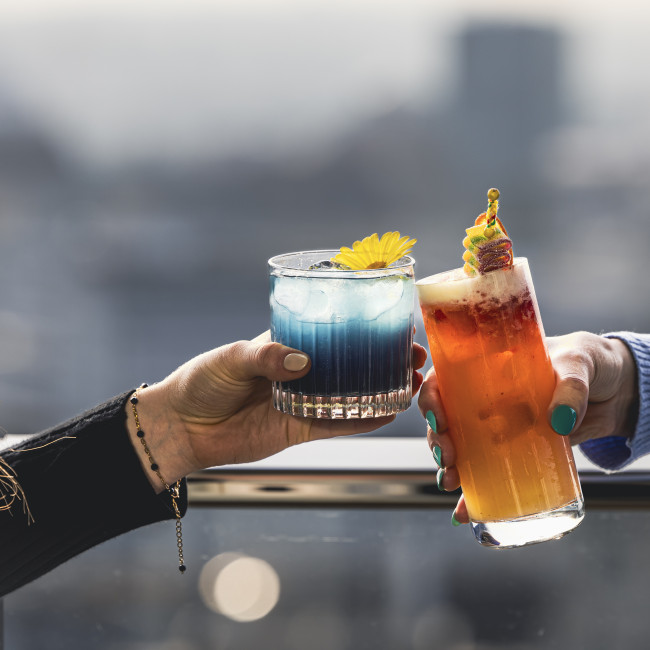 Zwei weibliche Hände stossen mit Cocktails an