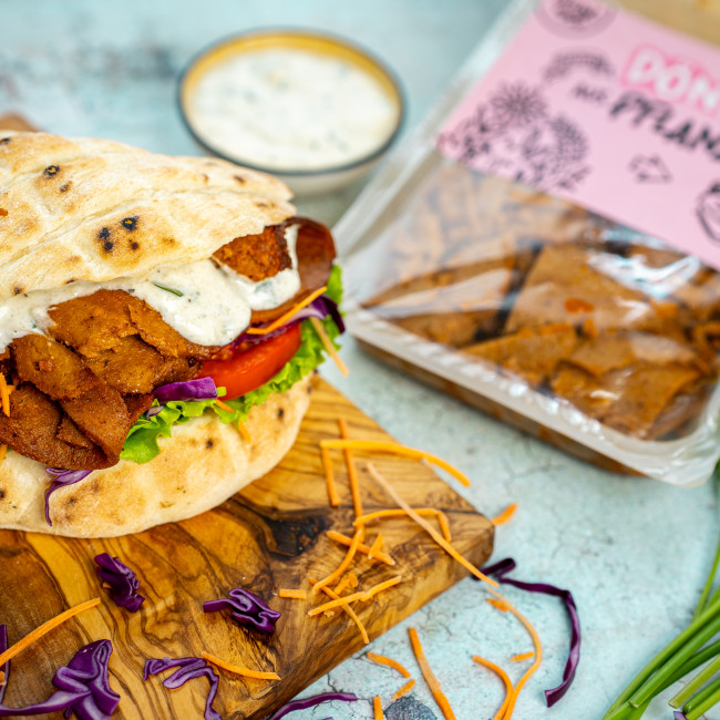 Pflanzenbasierter Döner mit Brot, dahinter eine Verpackung mit der Aufschrift Outlawz Food