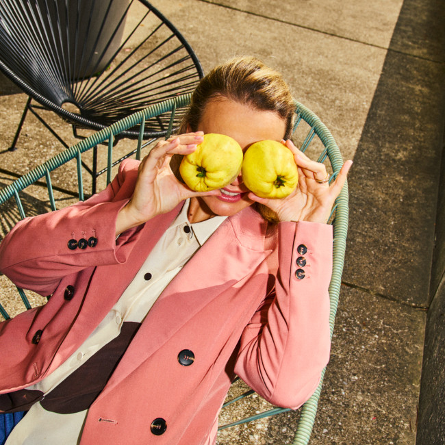Frau sitzt im Stuhl und hält sich zwei Äpfel über die Augen.