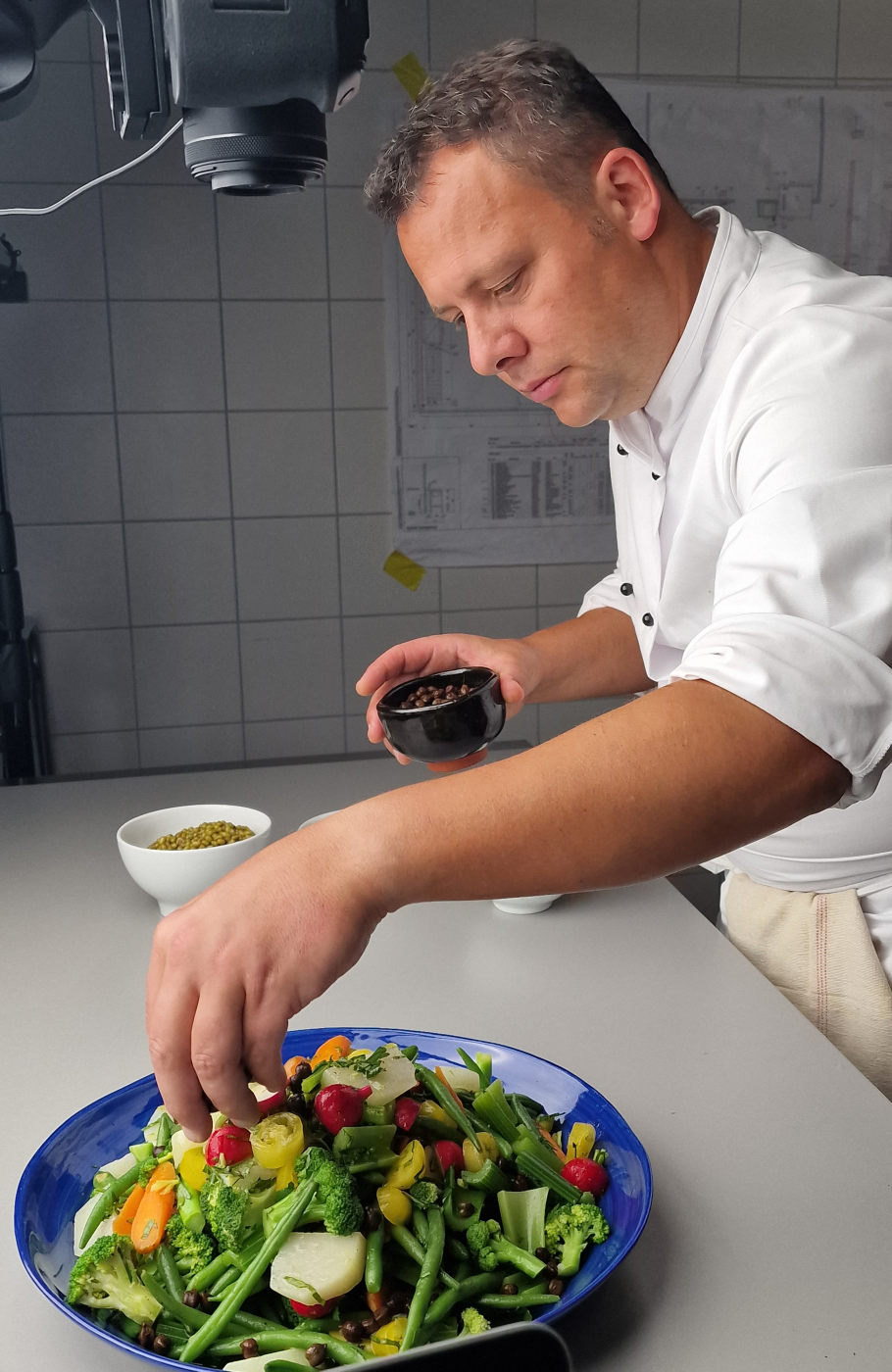 Koch mit weisser Kochjacke richtet Gerichte in Fotostudio an