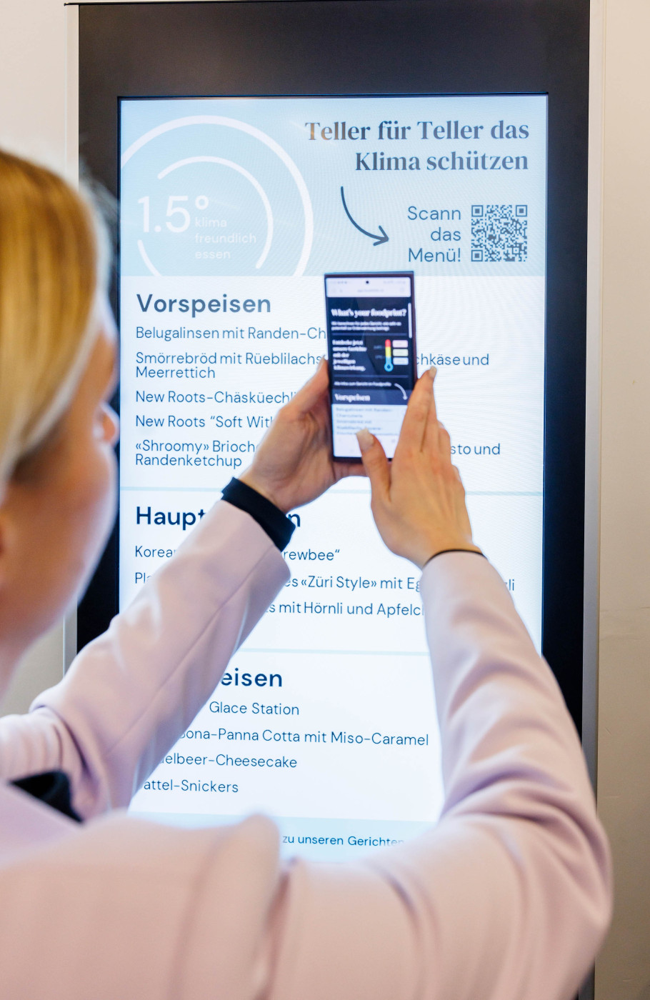 Frau scannt mit ihrem Handy einen digitalen Screen mit Klimainformationen