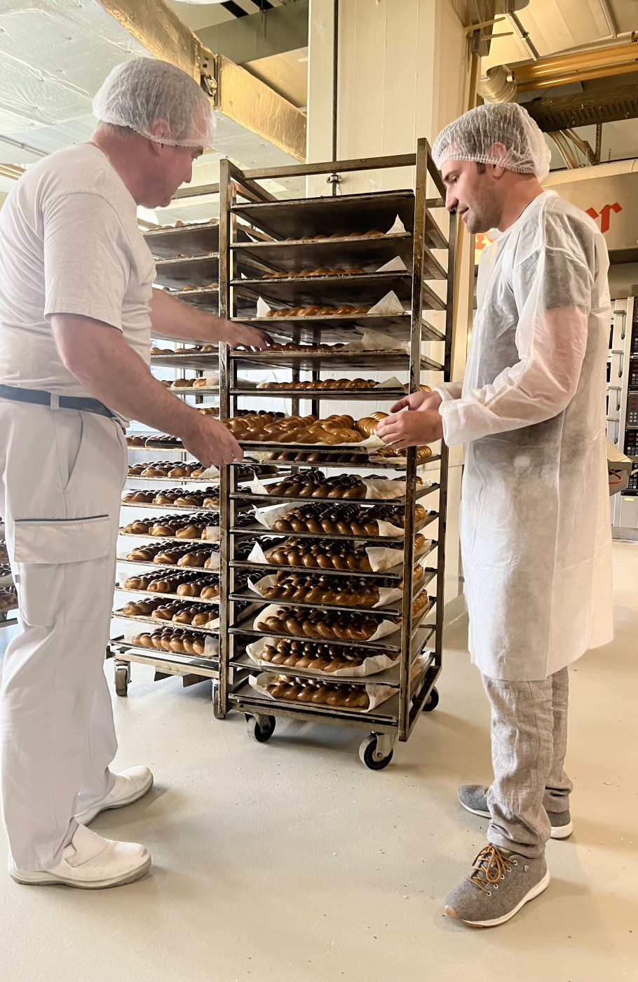 Zwei Bäcker in Uniform stehen vor einem Wagen voller Gebäck