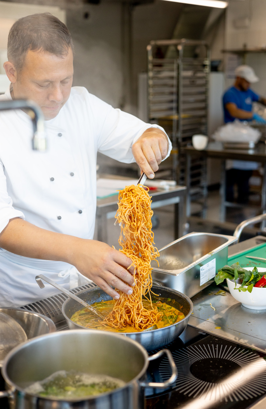 Mann in Kochjacke bereitet Spaghetti zu