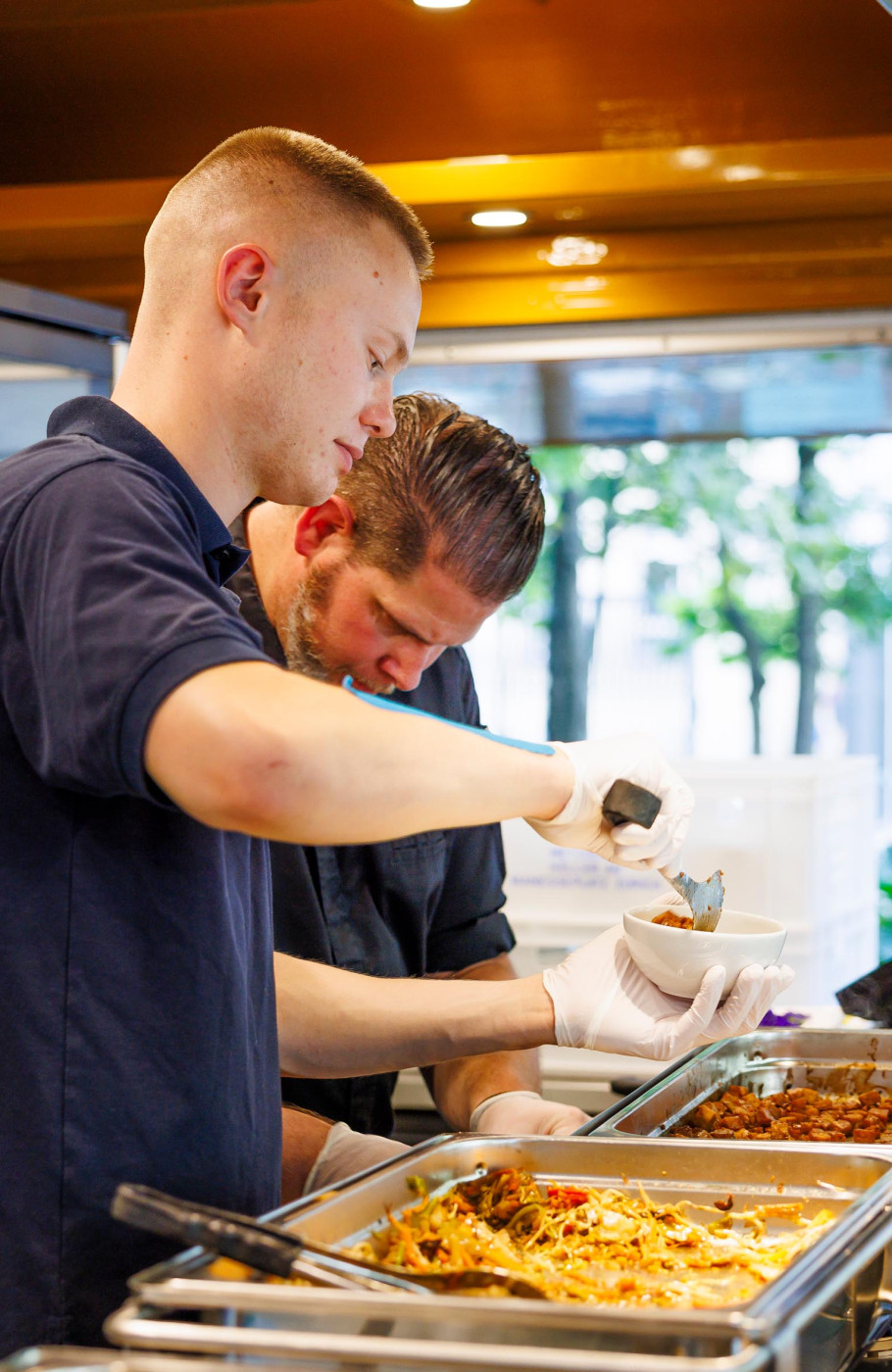 zwei Männer in einem Foodtruck mit blauen Shirts bereiten Essen zu