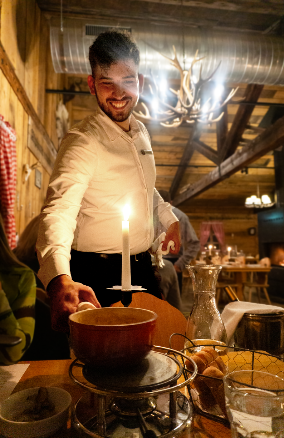 serviceangestellter setzt Fonduepfanne auf ein Rechaud auf dem gedeckten Tisch