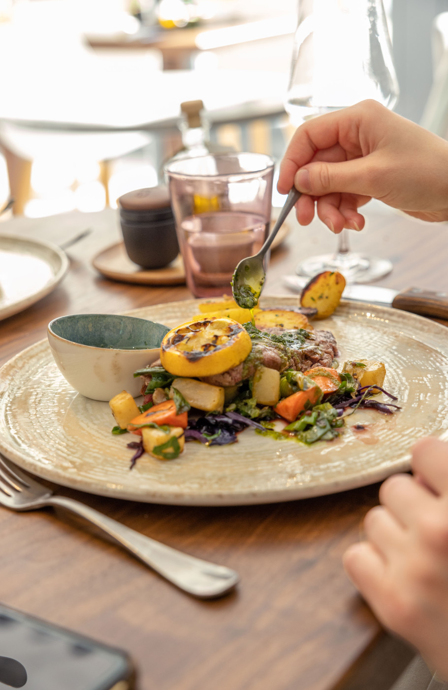 Teller mit weiblichen Händen, die Sauce auf ein Fleischgericht träufeln