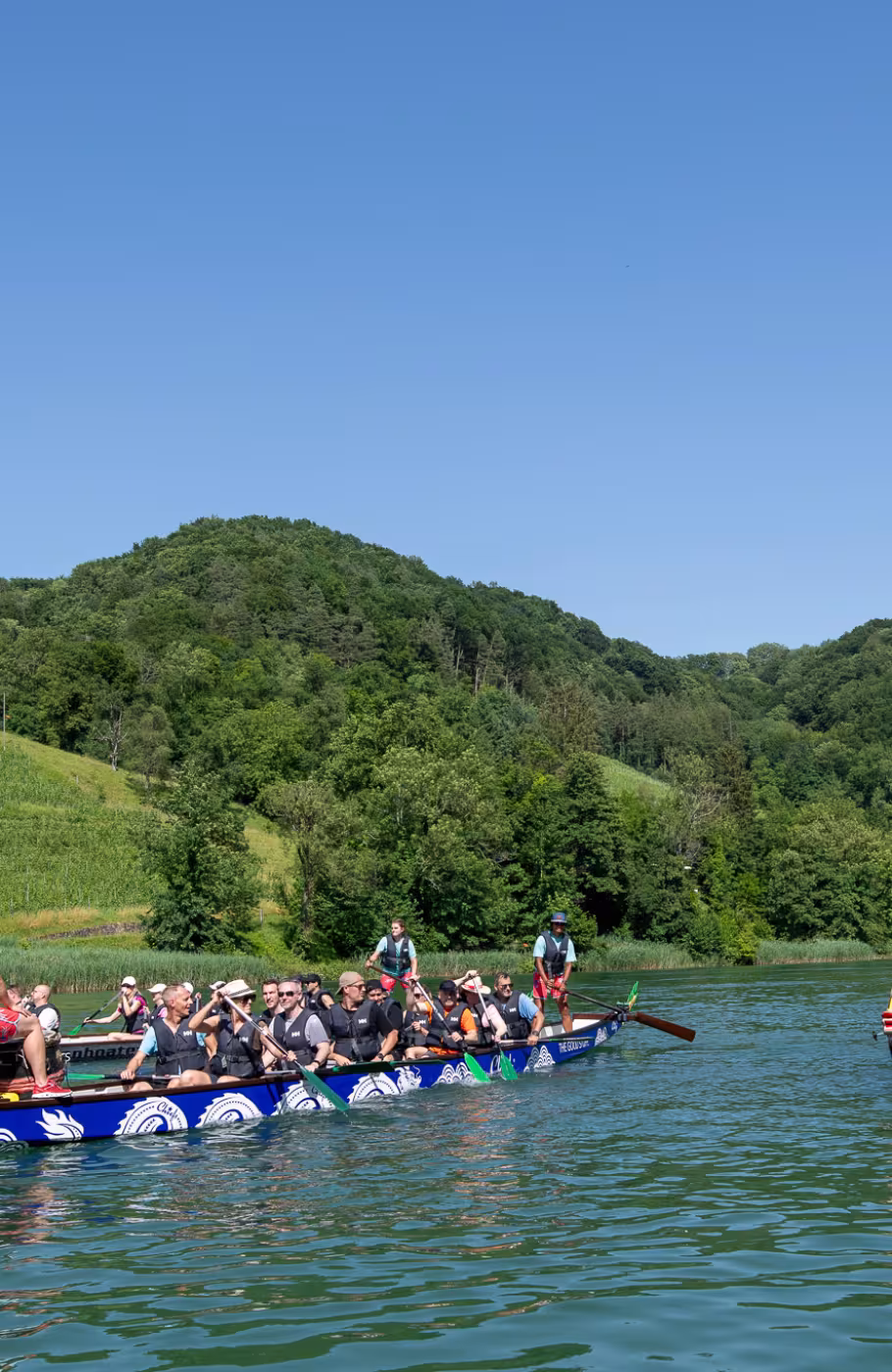 ZWei Drachenboote rudern mit mehreren Menschen über einen See