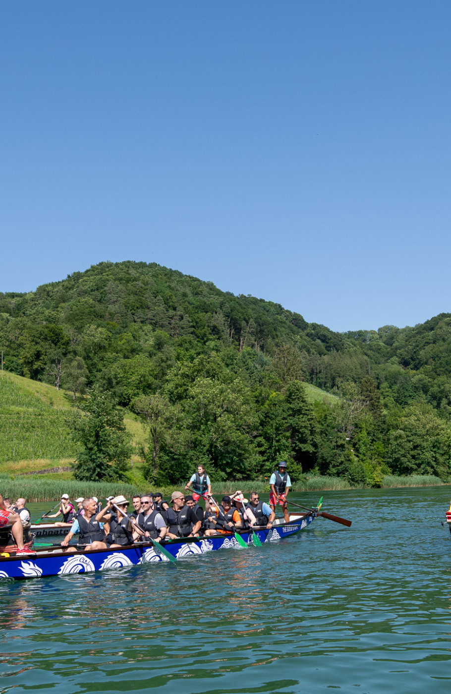 ZWei Drachenboote rudern mit mehreren Menschen über einen See