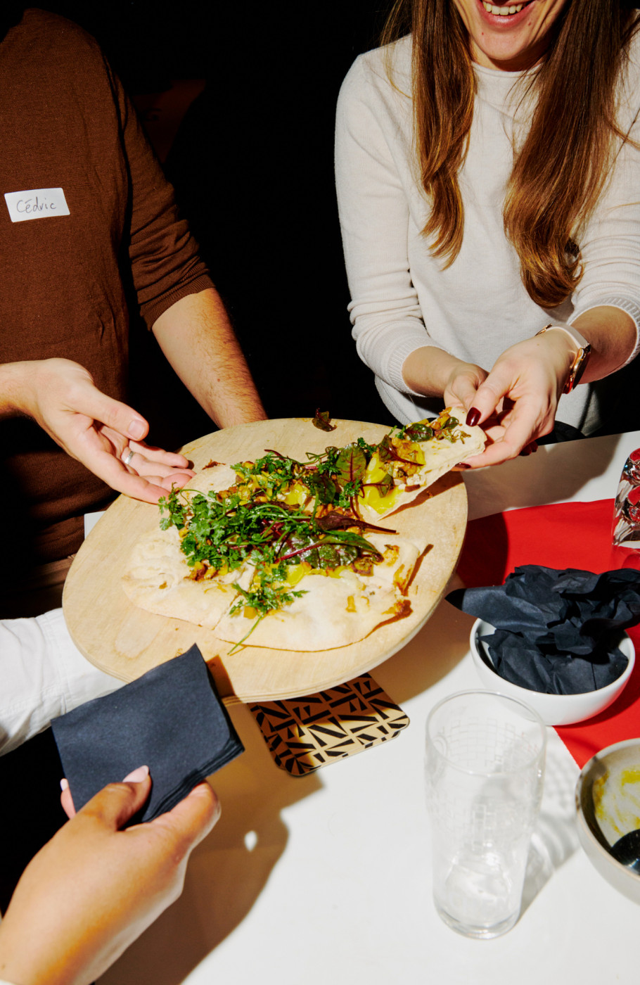 Drei Personen bedienen sich von einem Holzbrett mit Flammkuchen