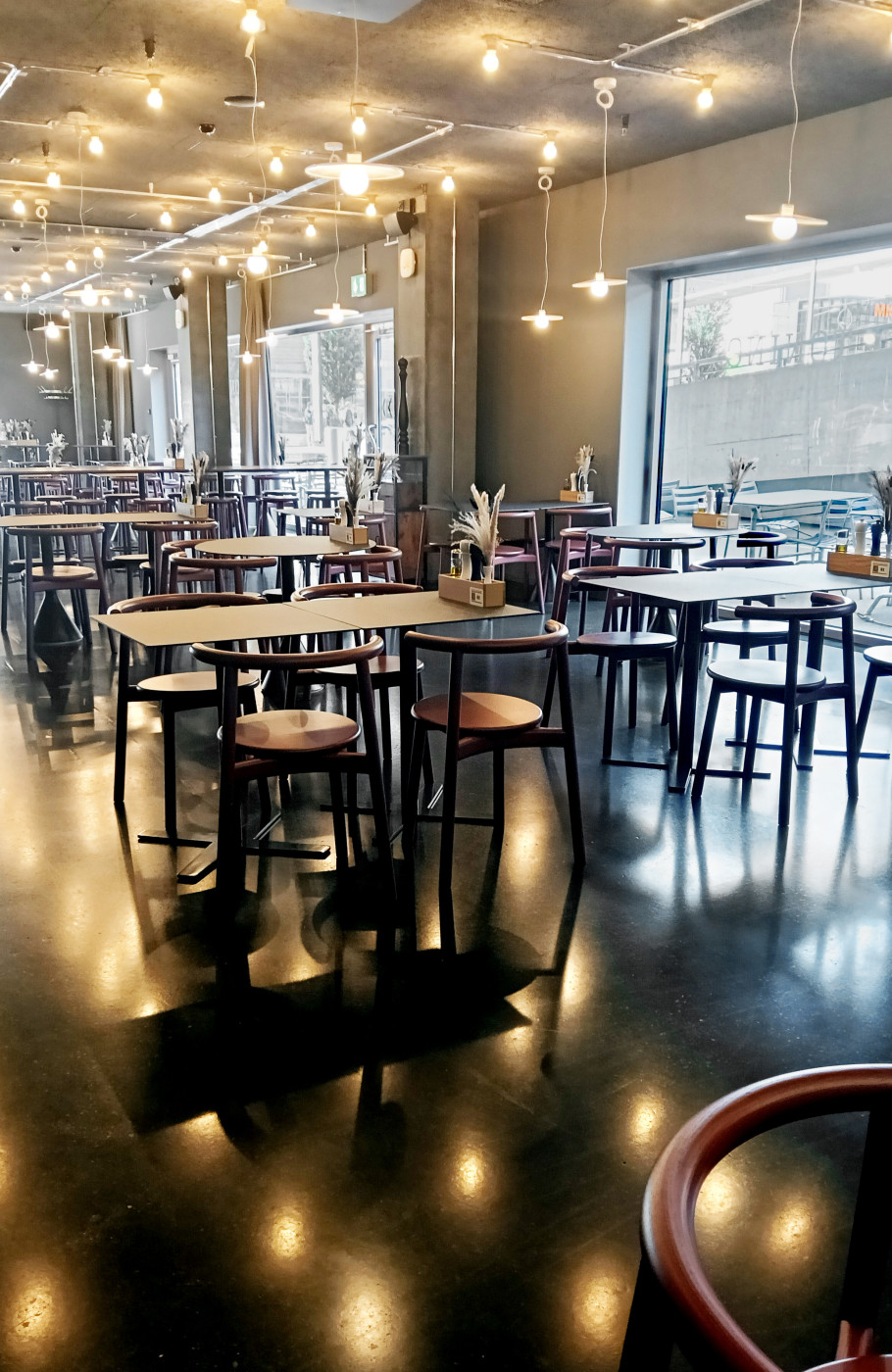 Heller Veranstaltungsraum der Eventlocation Bistro Tonino in Zürich mit moderner Beleuchtung, Hochtischen und grossen Fensterfronten.