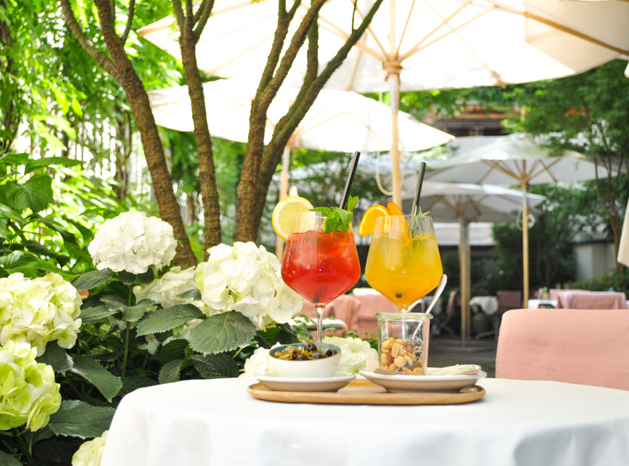 Weiss gedeckter Tisch auf Terrasse mit weissen Blumen zur linken und bunten Cocktails auf dem Tisch