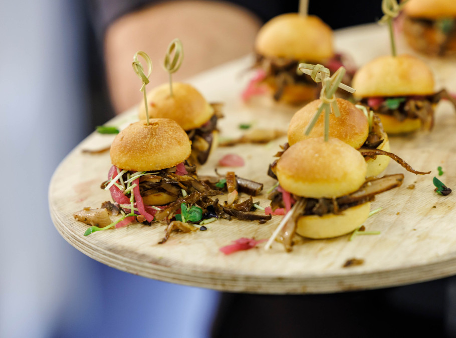 Mini Burger angerichtet auf einem Holzbrett gehalten von einem Servicemitarbeitenden