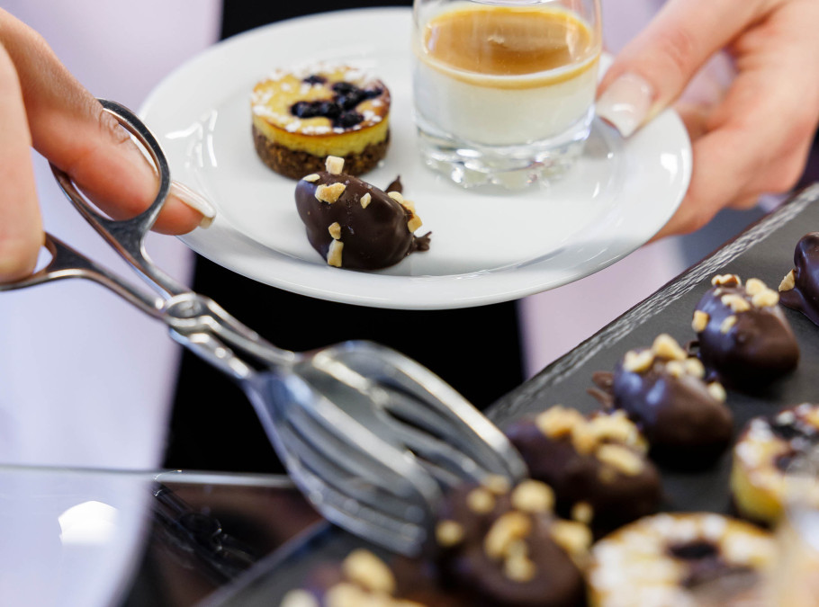 Veganes Dessertbuffet mit Blaubeerkäsekuchen und Brownies werden von einer Frau auf Teller geladen