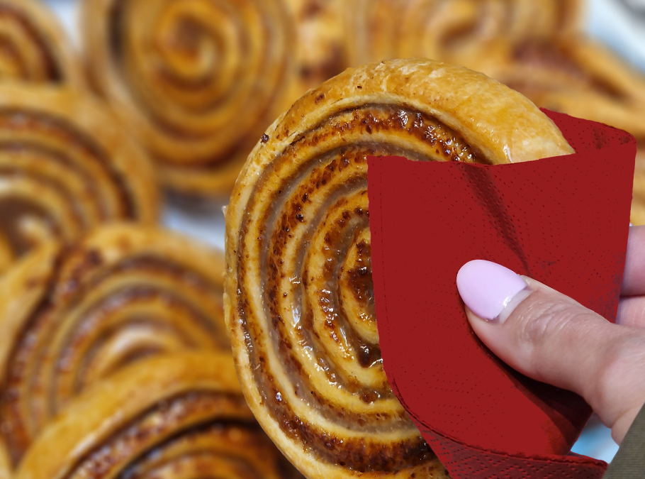 Zimtschnecken auf Silbertablett, weibliche Hand hält eine Zimtschnecke mit roter Serviette