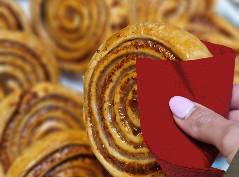 Zimtschnecken auf Silbertablett, weibliche Hand hält  eine Zimtschnecke mit roter Serviette