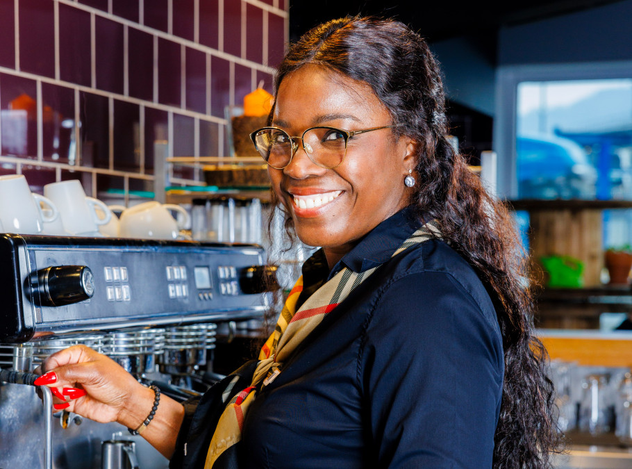 Frau steht an der Kaffeemaschine eines Restaurants und lächelt in die Kamera
